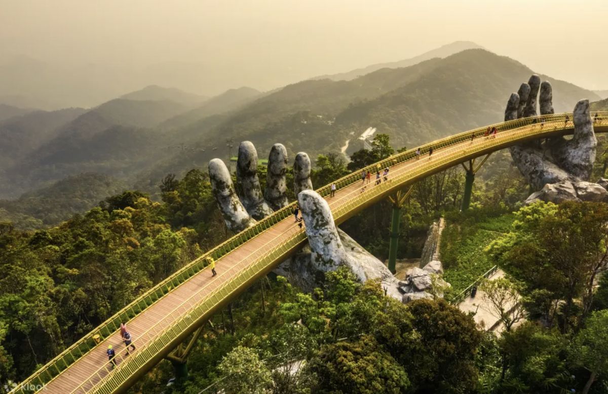 The Golden Bridge at Ba Na Hills, held aloft by two giant stone hands, set against forested hillsides in the clouds