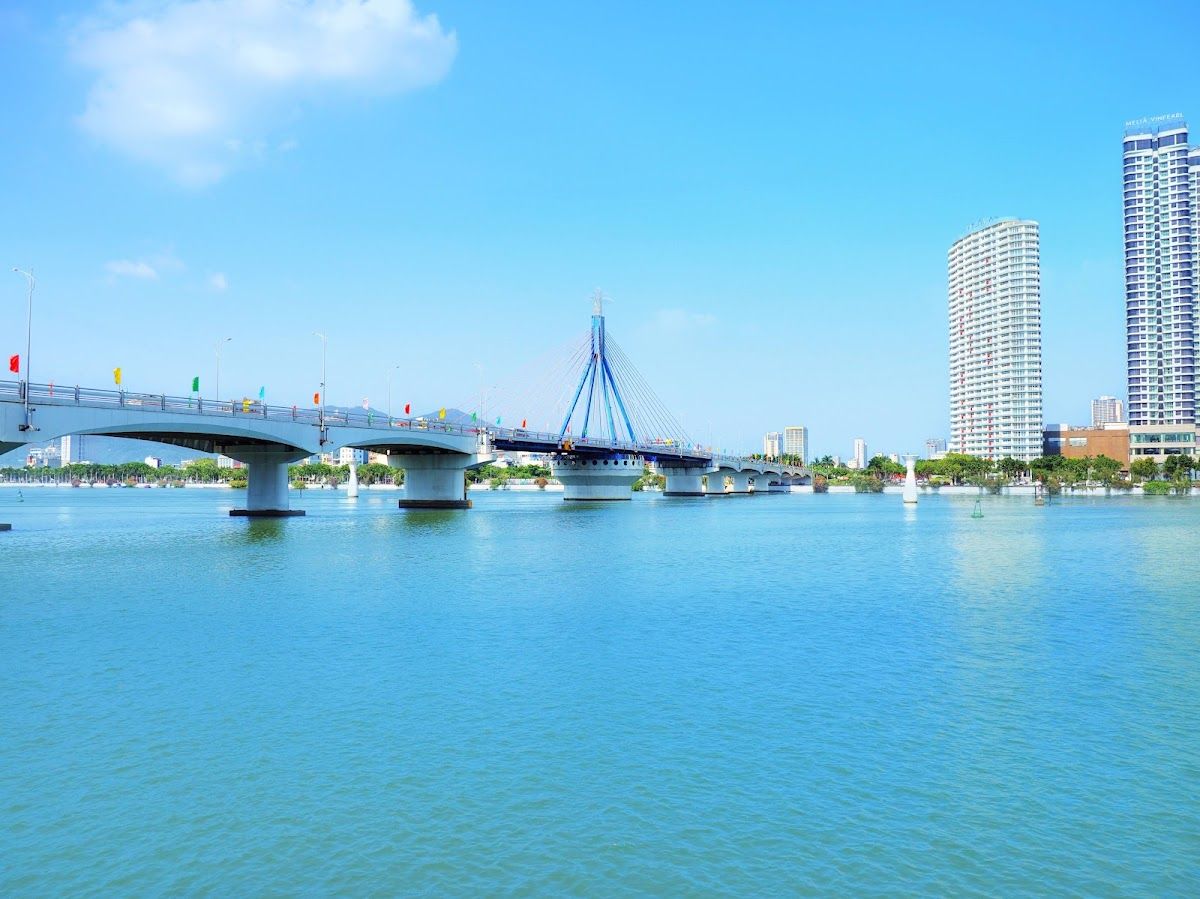 The Han River and Da Nang city skyline on a clear blue day, with a bridge spanning the water and high-rise buildings behind