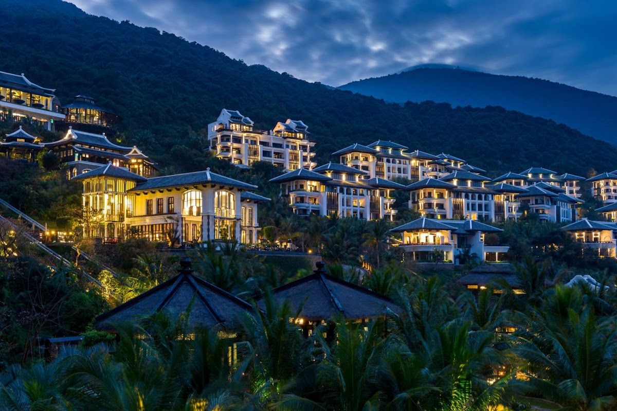 InterContinental Danang Sun Peninsula Resort at dusk, tiered luxury villas and pavilions cascading down a forested jungle hillside on Son Tra Peninsula