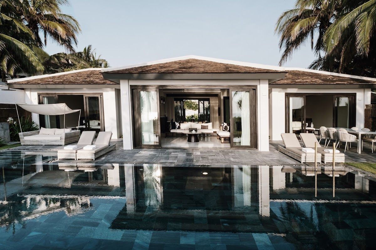 Private pool villa at TIA Wellness Resort on Non Nuoc beach in Da Nang, showing a large dark-tiled infinity pool with sun loungers and a modern open-plan villa building framed by palm trees