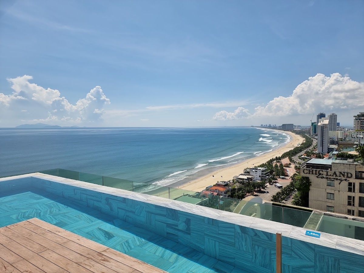 Rooftop infinity pool at A La Carte Danang Beach with My Khe Beach sweeping south and the East Sea stretching to the horizon beyond the glass balustrade