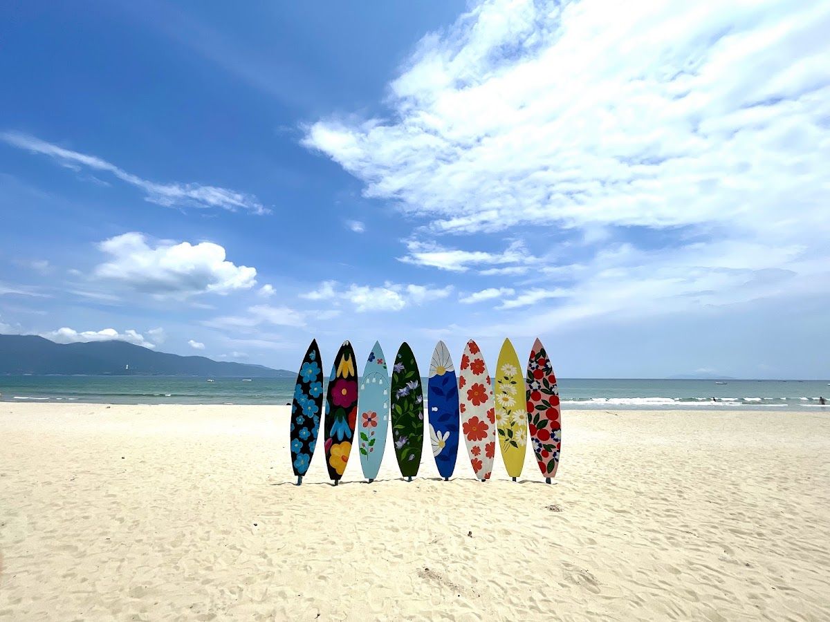 Colourful surfboards standing on white sand at My Khe Beach, Da Nang, with calm turquoise water and the Son Tra peninsula visible in the background