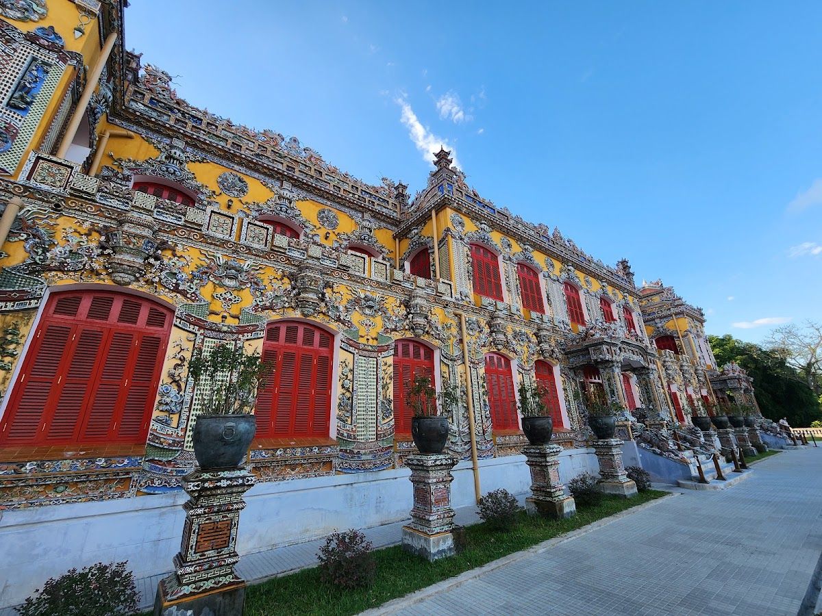 Ornate palace facade within Hue's Imperial City complex, covered in ceramic mosaic tiles with red-shuttered windows under a blue sky